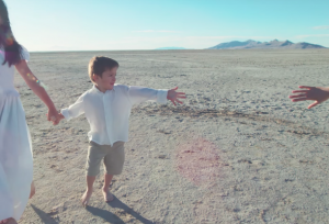 Latin American boy reaching for the hand of another child as part of the music video for "The Prayer," a Spanish - English cover by Kenya Clark and Alex Melecio